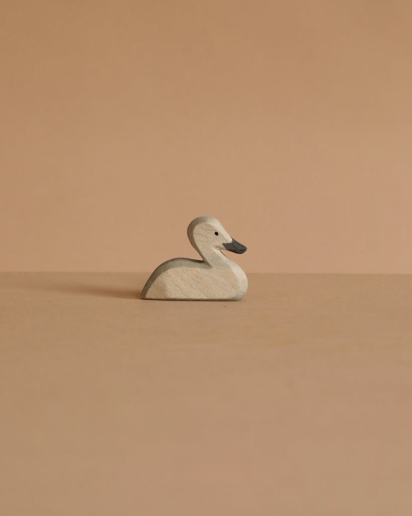 The small Ostheimer Swan, a light wooden figurine evoking handcrafted toys, rests on a beige surface with a matching beige background.