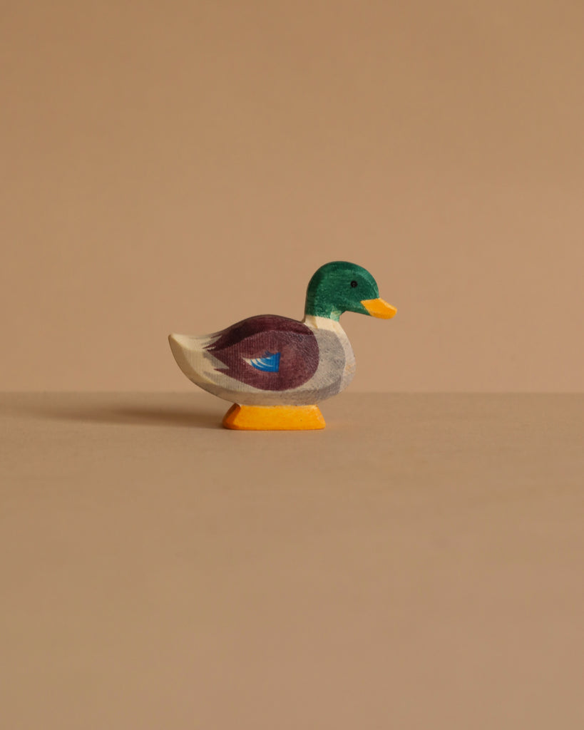 The Ostheimer Duck is a small handcrafted wooden figurine with a green head, yellow beak, brown and white body, and blue accent, displayed on a beige background—ideal for anyone who values safe, non-toxic toys.