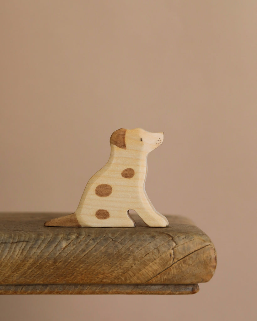 The Handmade Wooden Jack Russell, featuring brown spots, rests on a textured wooden surface against a beige background.