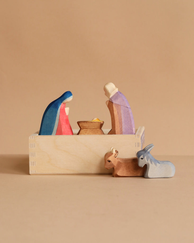 The Ostheimer The Holy Family Mini Set - 5 Pieces (Small) includes simple wooden figures of Mary, Joseph, baby Jesus in a manger, a brown donkey, and a gray ox—ideal for Waldorf toy collections.
