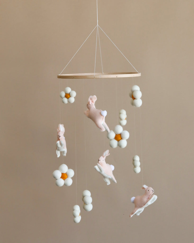 A nursery mobile featuring plush jumping bunnies and white and yellow balls hanging from a white frame against a soft beige background.