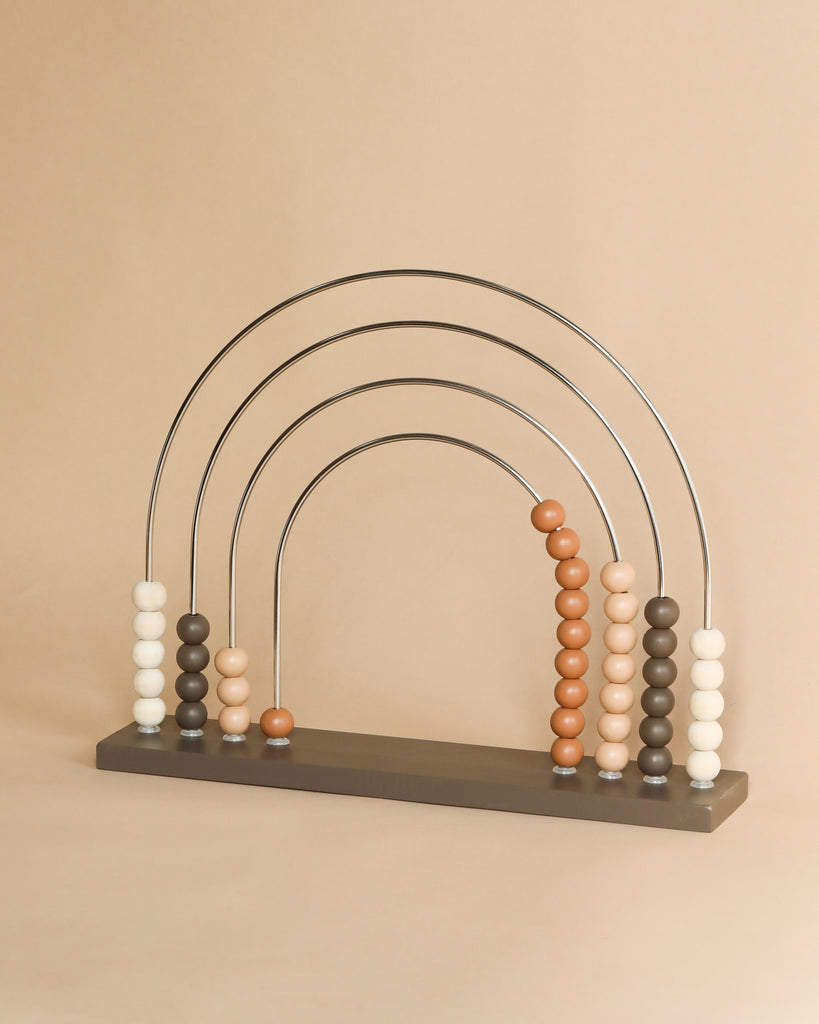 A Large Abacus Rainbow - Dark with a rainbow-shaped top, designed to enhance motor skills, featuring beads in shades of white, peach, and brown, set against a light beige background.