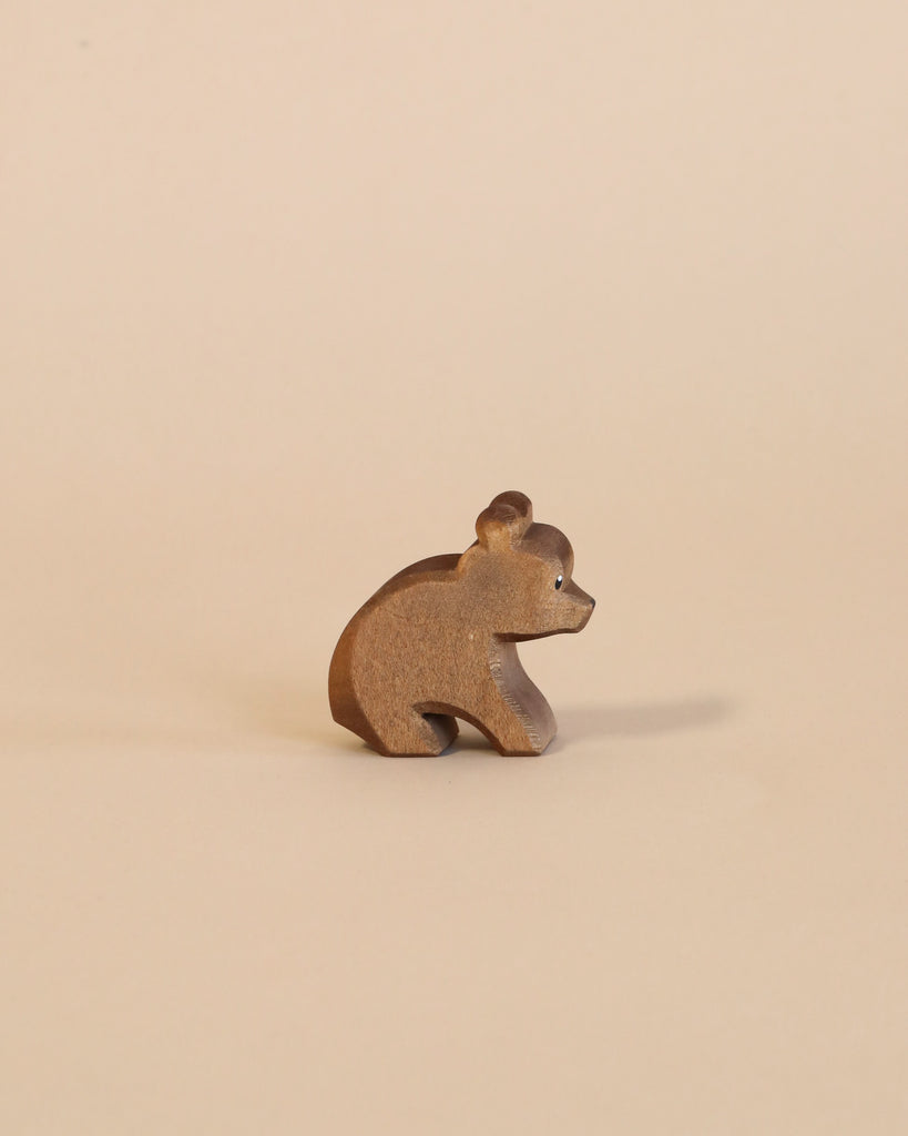 A small, handcrafted Ostheimer Small Bear - Sitting figurine stands against a plain, beige background, with the bear in a sitting position and its head turned to the side.