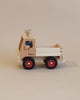 A handcrafted Fagus Wooden Unimog Truck with red wheels and a blue peg figure driver inside, set against a plain beige background.