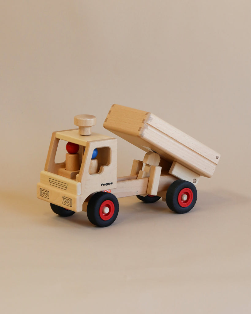A handcrafted Fagus Wooden Dump Truck with red wheels and a movable dump bed, displayed on a plain background.