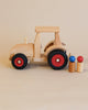A handcrafted Fagus Wooden Modern Tractor with red rubber tires, beside two wooden blocks and a pair of small blue and red balls, set against a neutral background.