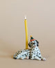 A Dalmatian Cake Topper with a party hat next to a tall, yellow candle, against a soft beige background, showcases heirloom quality craftsmanship.
