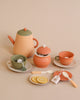 A handmade wooden tea set of herbal tea ware including a teapot, sugar bowl, cups, and plates, all in soft pastel colors, accompanied by lemon slices and tea bags.