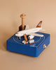 A miniature replica of an Airport Music Box sitting on a blue platform with a runway design, surrounded by small wooden models of buildings and vehicles, all crafted from sustainably sourced wood.