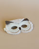 An elegant, white Donsje Tieri Mask | Owl with furry texture and metallic leather details, placed on a light brown background.