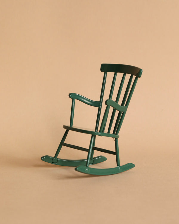 A small, Maileg dark green rocking chair designed for a mouse stands against a plain beige background, emphasizing its simple, classic design.