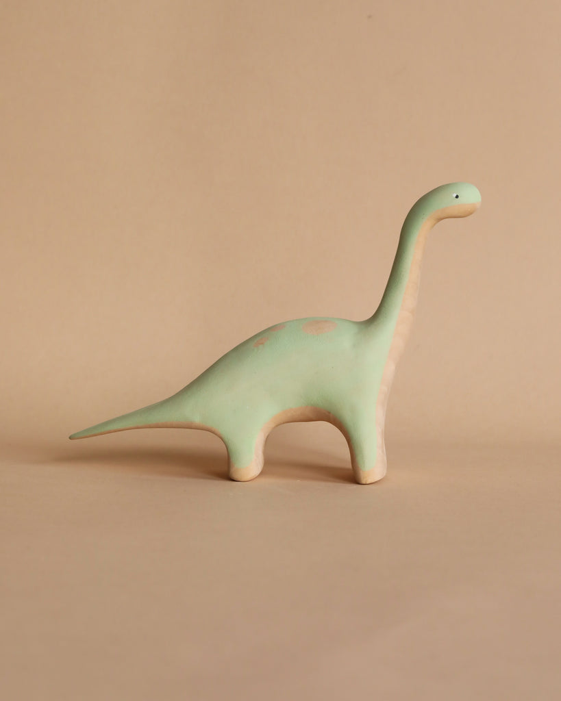 A small, handmade wooden Brachiosaurus dinosaur figurine with a long neck and tail, standing against a plain beige background.