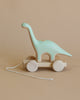 A pale green Handmade Wooden Brachiosaurus Dinosaur push toy with built-in magnets, set against a light brown background.