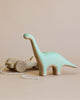 A Handmade Wooden Brachiosaurus Dinosaur Push Toy With Built-In Magnets on wheels with a pull string, handcrafted and painted in pastel green using non-toxic child-safe paint, displayed against a plain beige background.