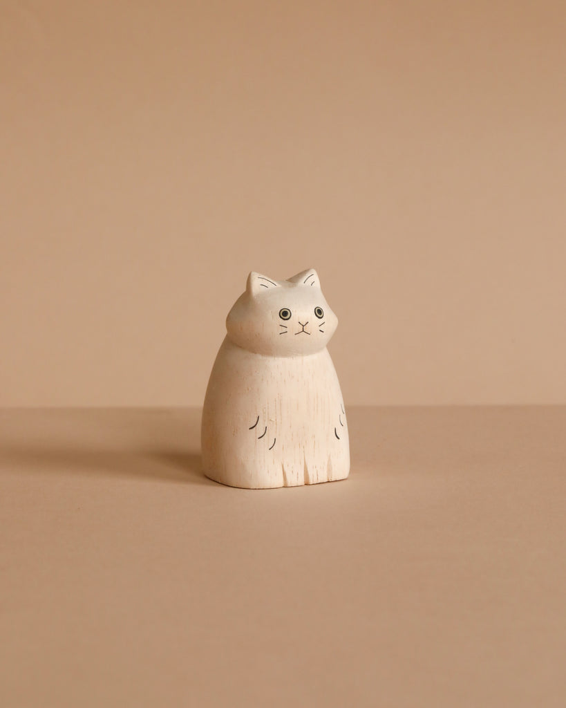 The Handmade Tiny Wooden Animals - Long Haired White Cat is a small, minimalist white cat figurine with black features, handcrafted by Bali artisans from Albizia wood, displayed on a beige surface against a beige background.
