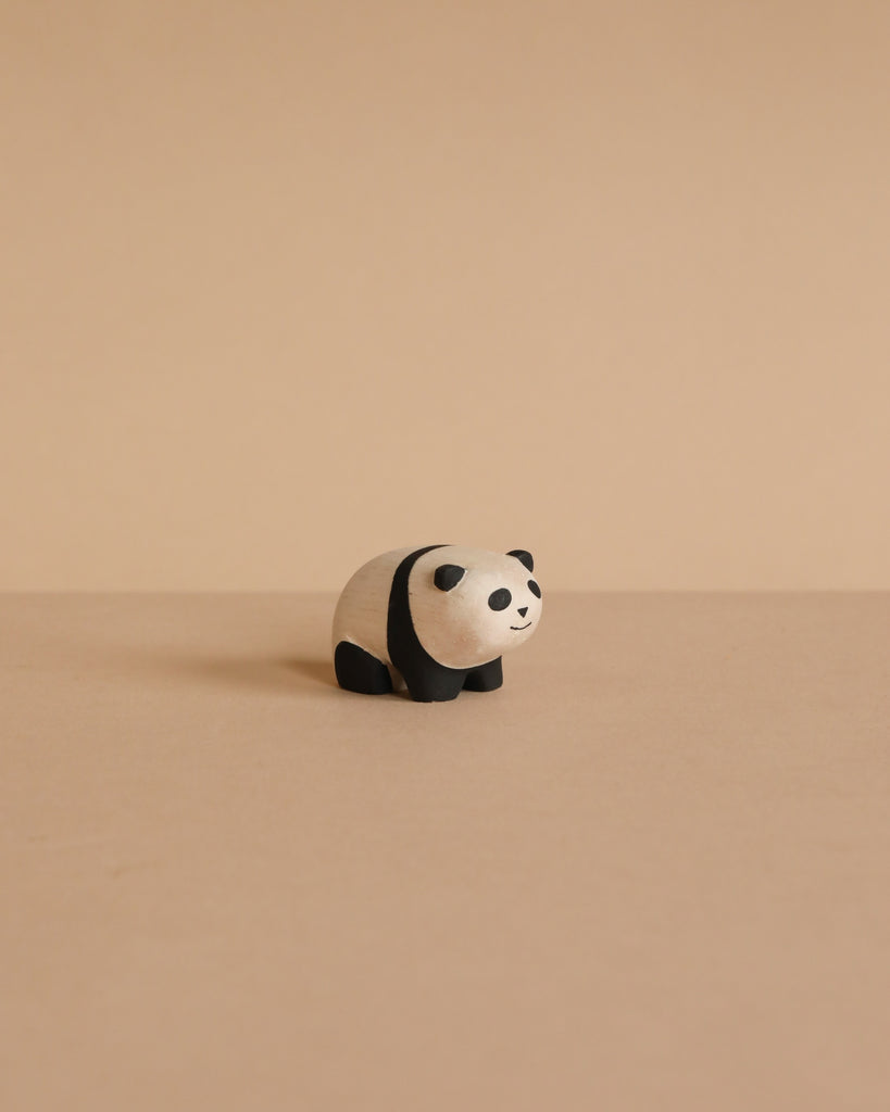 The Handmade Tiny Wooden Panda Child, crafted from Albizia wood, stands on a beige surface with a matching background, highlighting the charming artistry of Bali's skilled artisans.