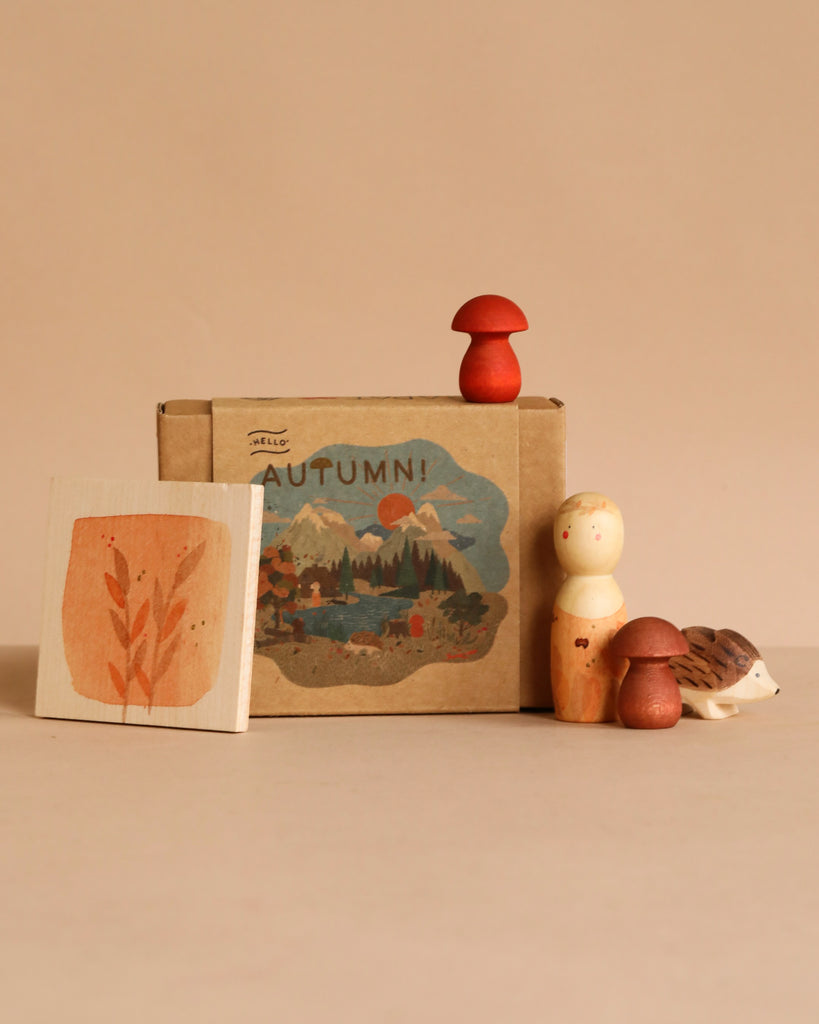 The Hello Autumn Set (Grapat X Ostheimer Limited Edition) features a "AUTUMN!" box with a mountain scene and leaf painting, plus exclusive wooden figurines—a person, mushrooms, and hedgehog—arranged on a beige background.