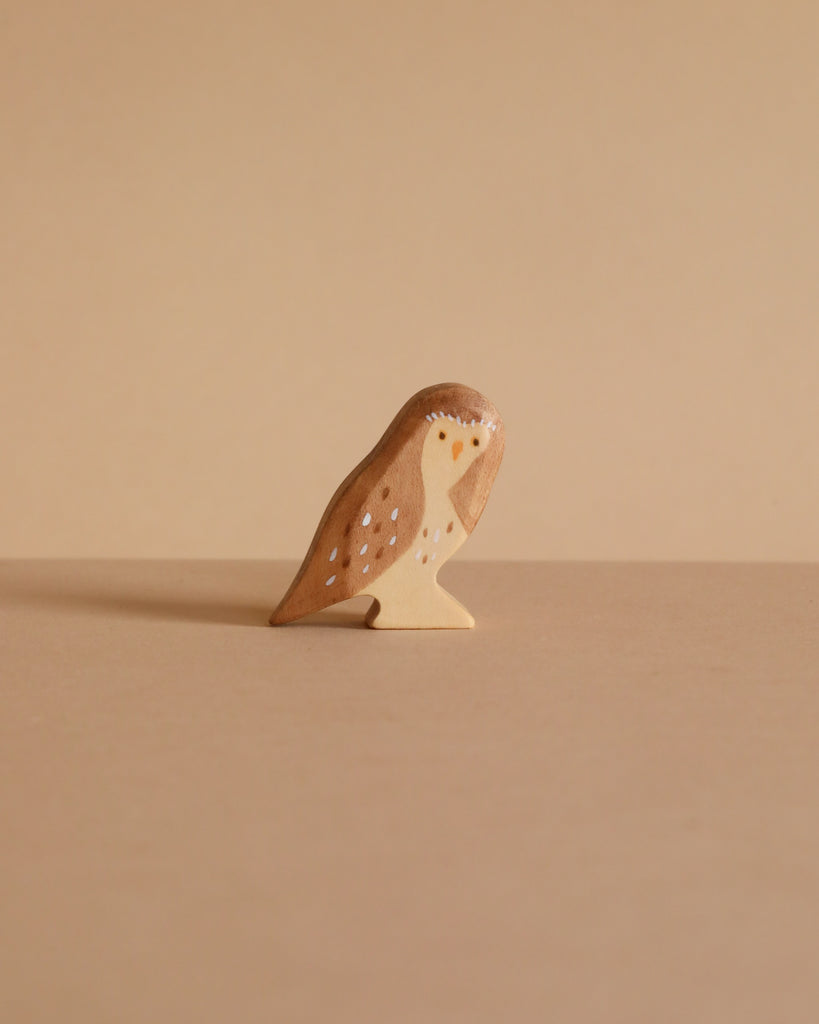 The Handmade Wooden Little Owl, a small figurine crafted from sustainable hardwood with simple painted details using plant-based stains, stands on a flat beige surface against a plain beige background.