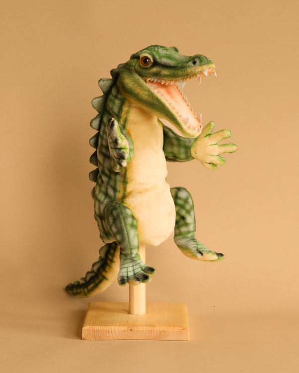 A whimsical model of an Alligator Puppet standing upright on a wooden base, featuring detailed scales, expressive eyes, and an open mouth. The background is a plain beige color. This handcrafted