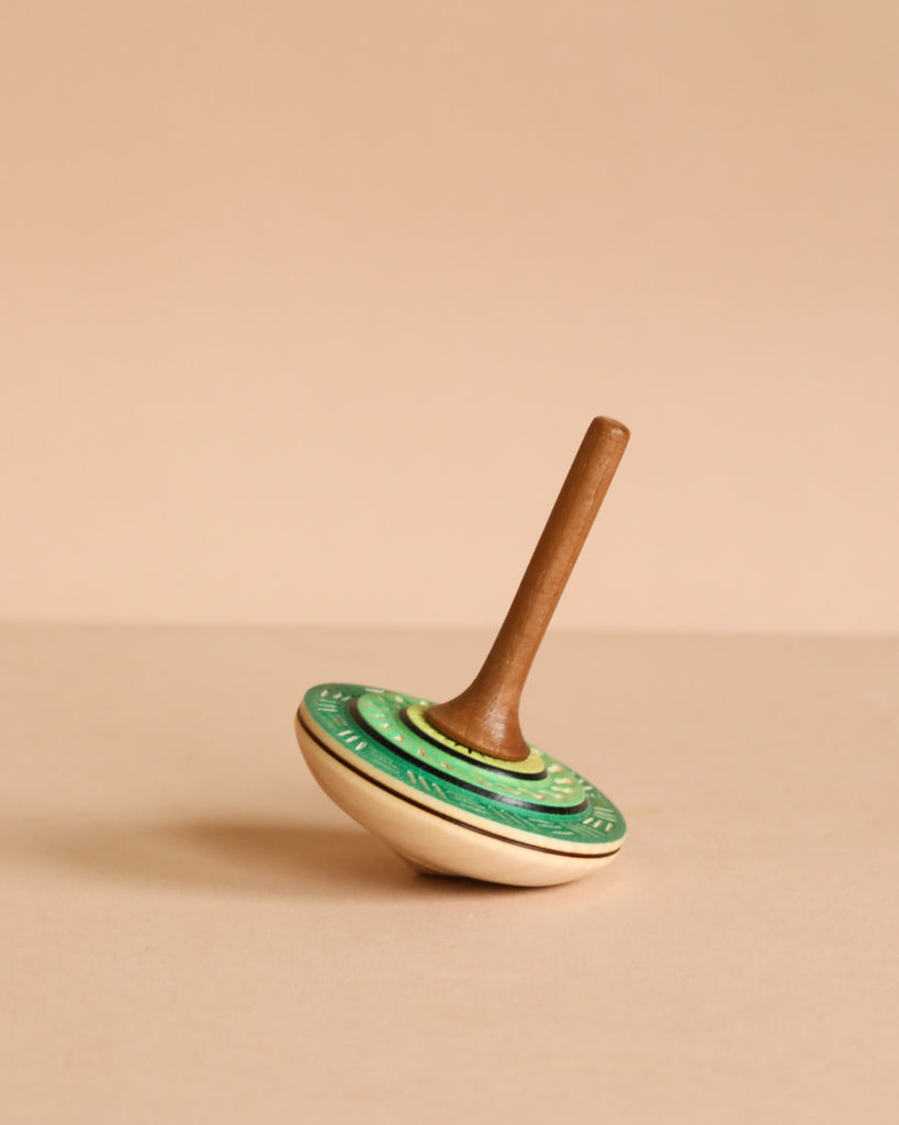 The Mader Bonbon Spinning Top - Green features a charming green and cream wooden design, displayed on its side against a beige background, highlighting the timeless appeal of this classic Austrian toy.