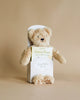 A Slumberkins Honey Bear Kin with light brown fur peeking out of a white box labeled "Honey Bear, I'm grateful for you" against a neutral beige background.