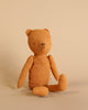 A worn, tan Maileg Teddy Mum with a vintage look sits upright against a light beige background, showing signs of aging and love with a slightly frayed texture and stitched features.