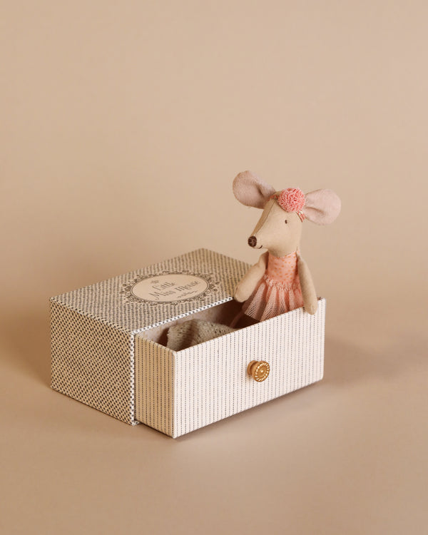A small Maileg Dancing Mouse in Daybed toy wearing a pink dress and a bow, sitting inside an open fabric-lined box, against a plain beige background.