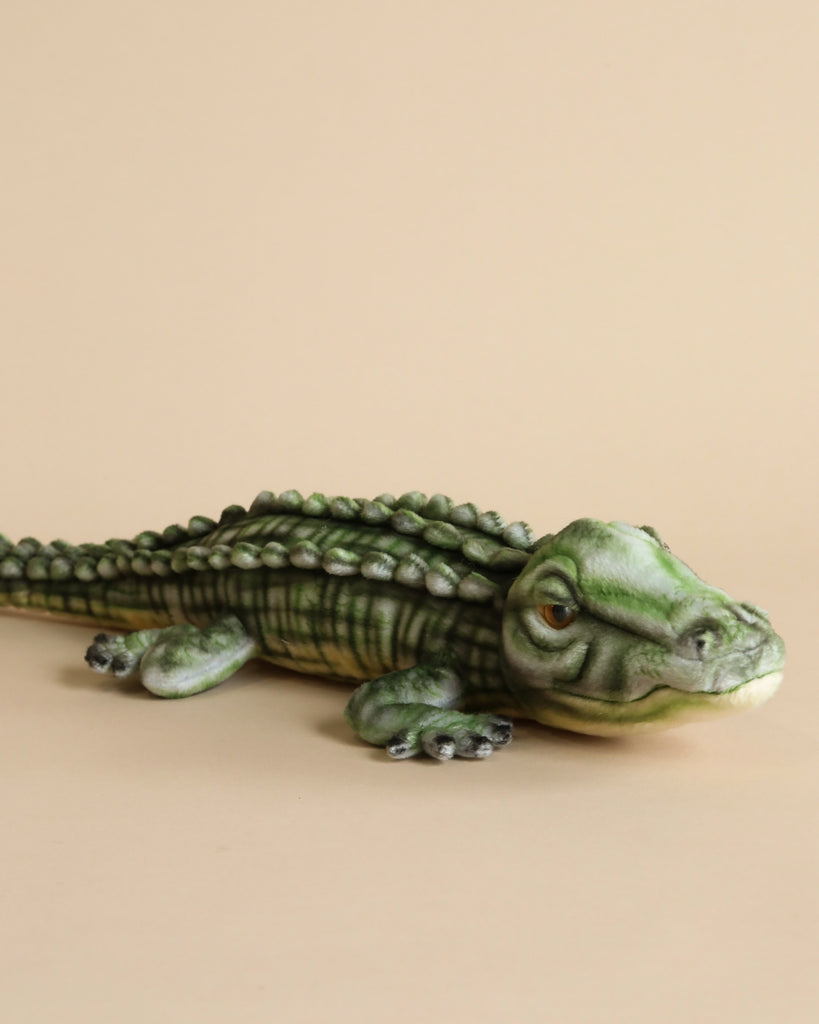 A realistic plush model of an Alligator Stuffed Animal lying down on a plain beige background. The figure is highly detailed, capturing even the textures of its scales.