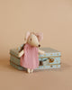 A Maileg Angel Mouse in Metal Suitcase wearing a pink dress and a backpack stands in front of a mint colored suitcase with a star pattern. The background is a solid light beige color, creating a soft, whimsical scene.