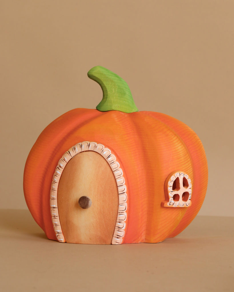 The Bumbu Handmade Wooden Haunted Pumpkin Cottage Set features a small wooden pumpkin house with a green stem, door, and window—perfect for Montessori imaginative play. Displayed on a plain beige background.