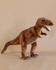 A T-Rex Stuffed Animal standing against a plain beige background, featuring detailed stitching and a realistic design with sharp white teeth and focused eyes. This artisan hand-sewn figure captures the