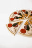 A Sabo Concept Wooden Pizza sliced into eight pieces, each topped with various colorful play toppings such as mushrooms, tomatoes, and leaves, arranged on a white background.