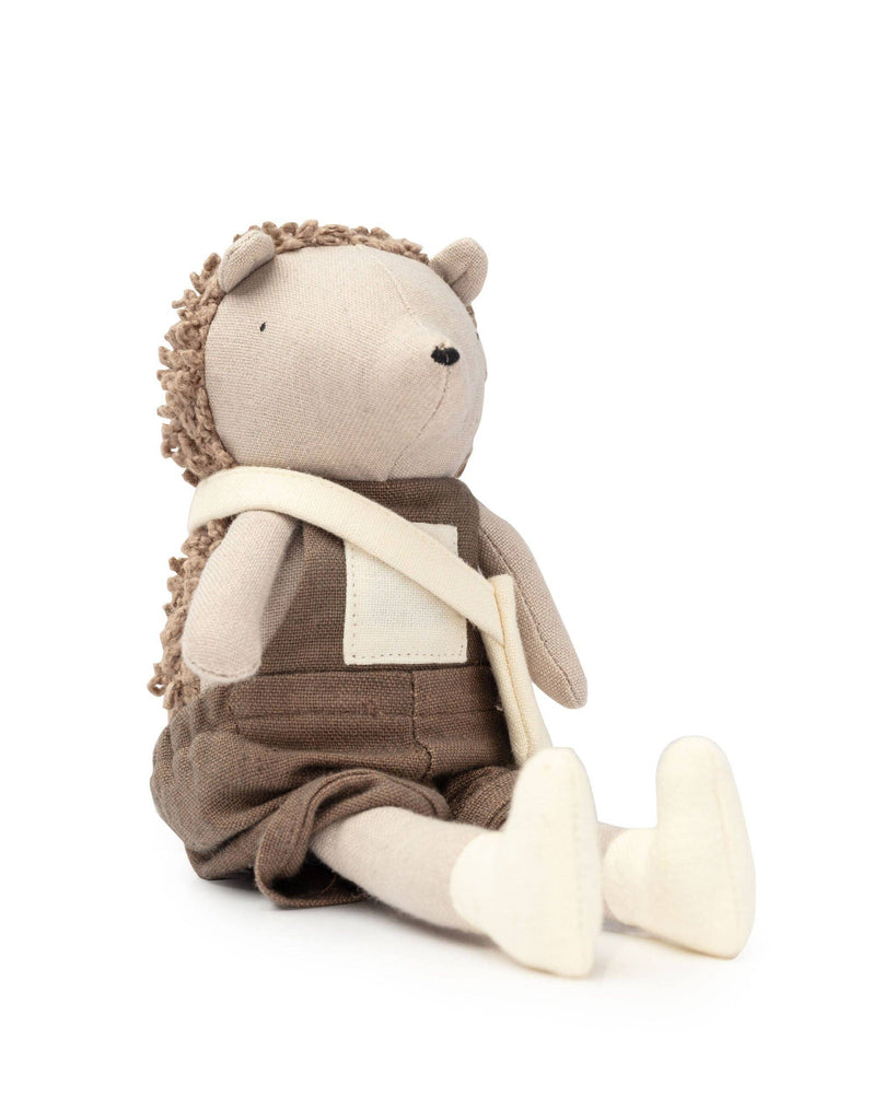 Harold The Hedgehog is a plush toy from our Hedgehog Family series, perfect for secret garden adventures. It features a textured back and wears a brown outfit with a cream crossbody strap. Sitting upright with extended legs, Harold is among the coziest companions around.