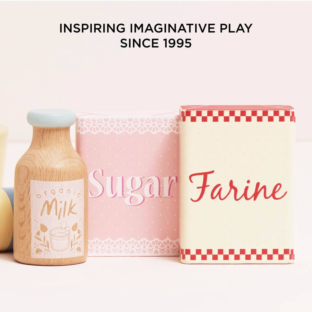 The Bakers Mixer Set & Accessories includes a wooden toy milk bottle and two labeled boxes, “Sugar” and “Farine”—ideal for pretend play in any toy kitchen. The text above reads, "INSPIRING IMAGINATIVE PLAY SINCE 1995.