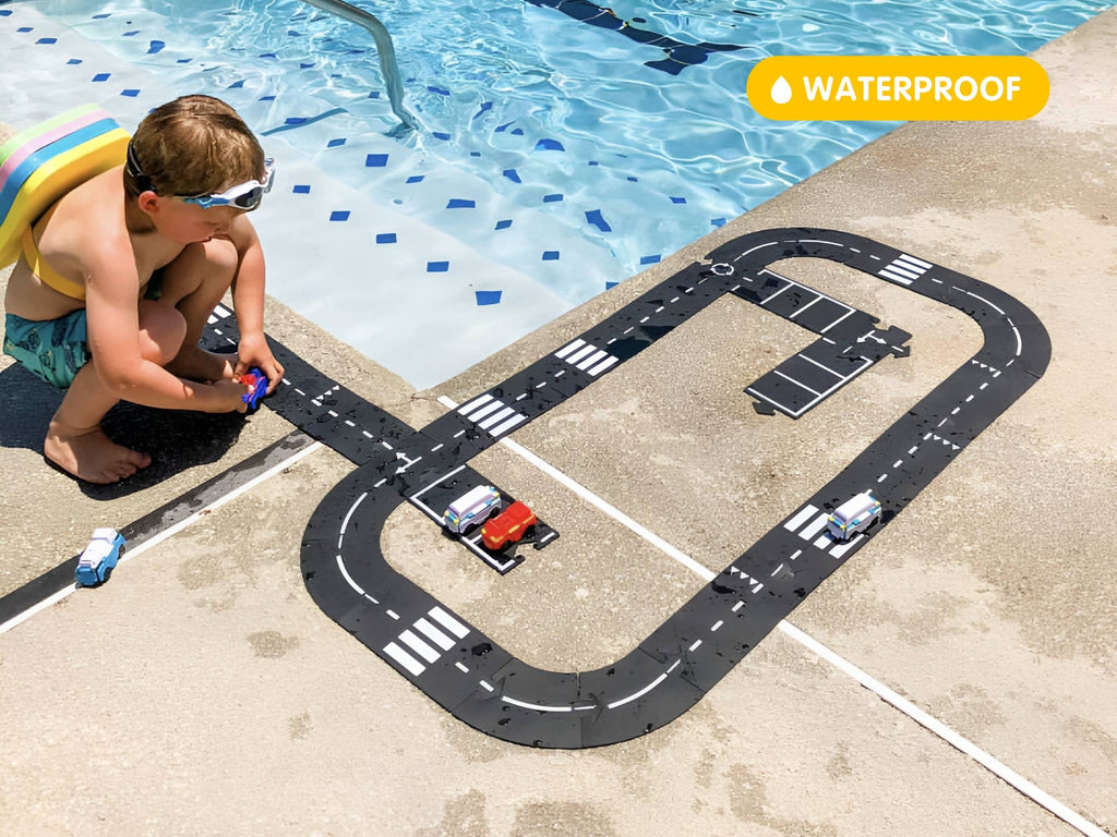 A child wearing swim goggles plays with toy cars on the WaytoPlay: Extra Long Flexible Road Set - King of the Road by a pool, inspiring imaginative play. A yellow label in the top right corner displays "WATERPROOF.
