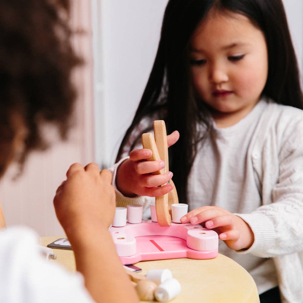Two young children play together at a table with the Wooden Dentist Set. One child is focused on holding and stacking the wooden pieces, encouraging imaginative role play.