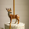 A small, decorative Stag Cake Topper with hand-painted details and a crown, standing on top of a white, speckled birthday cake, partially obscured by a yellow candle.