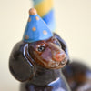 Close-up of a hand-painted Dachshund Cake Topper wearing a blue polka-dotted party hat, focusing on its detailed face with vibrant colors.