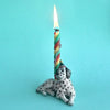 A Dalmatian Cake Topper with a tall, multicolored spiral candle lit on its head, set against a plain turquoise background, serves as a collectible keepsake.