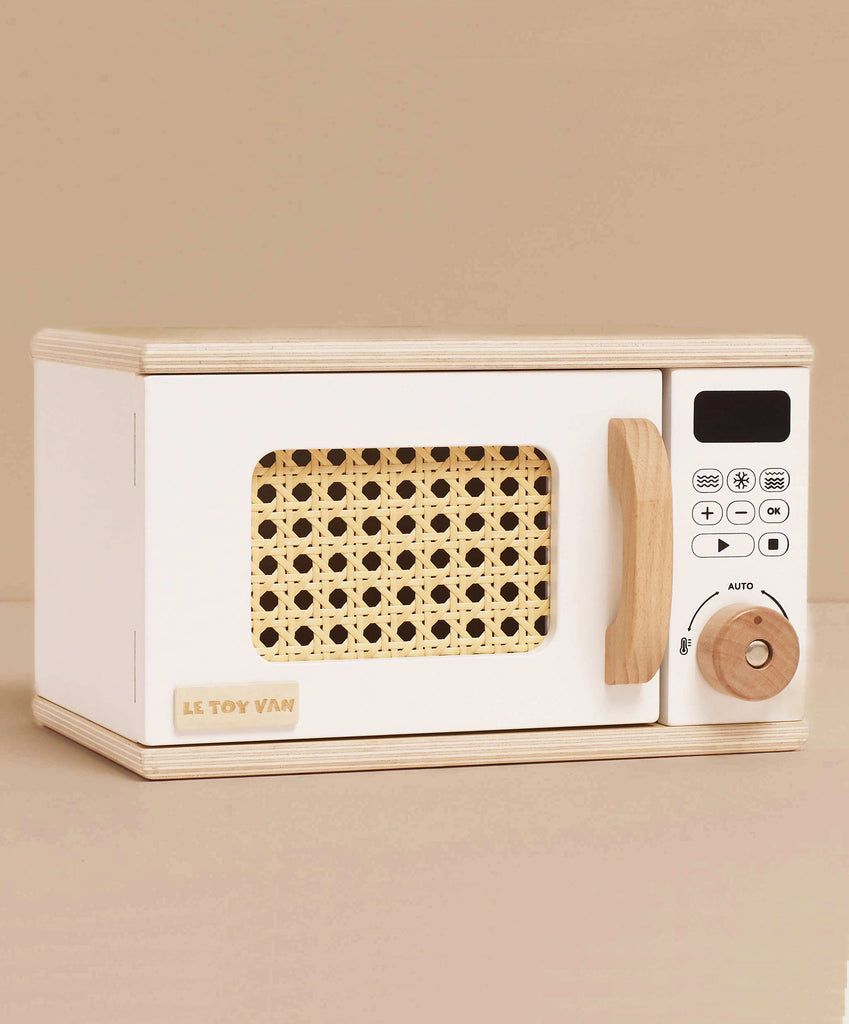The Wooden Microwave (ships in one week) is a small, sustainable wood toy with a white body, natural handle and knob, woven rattan-look window, and a control panel featuring printed buttons and a digital display—perfect for play kitchens.