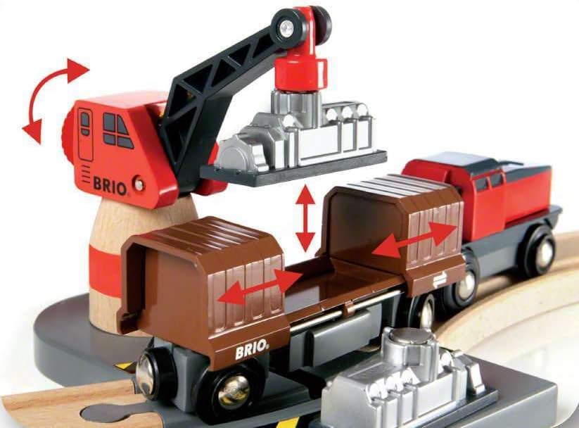 A BRIO World Train Set Cargo Harbour Set red crane lifts a silver engine part from a brown train car, while a red engine waits on wooden tracks. Red arrows indicate the movements of the crane and cargo doors.