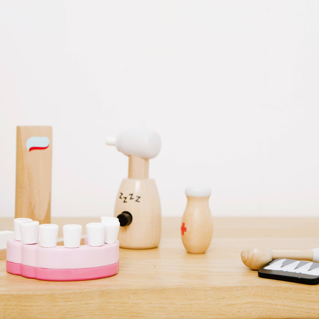 The Wooden Dentist Set includes a model of teeth, dental drill, medicine bottle, and other tools—ideal for role play—displayed on a light wooden surface with a plain white background.