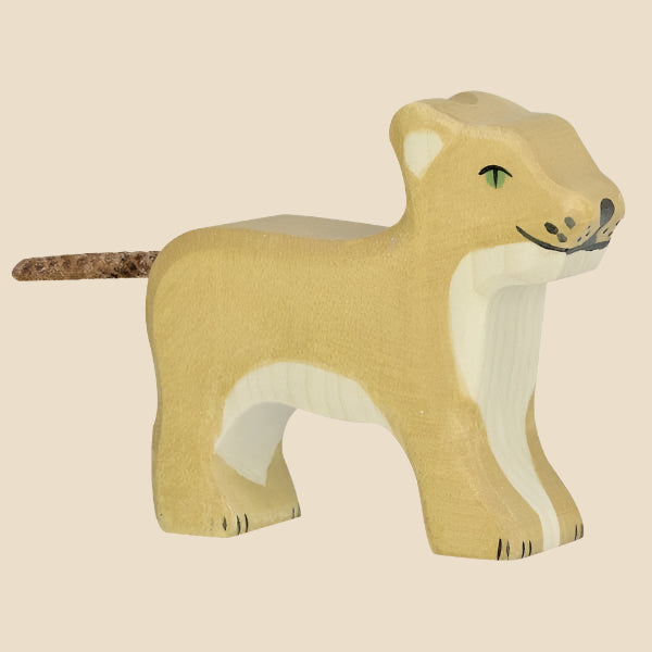 The Holztiger Lion Cub is a handcrafted wooden figure painted light brown with white accents, green eyes, and a cork-like tail. Made in Europe, it stands on all fours and ships in one week.