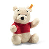 A Steiff plush toy bear with cream-colored fur, wearing a red shirt, sitting on a white background. The bear appears soft and cuddly, with a friendly expression and distinctively features a "Button in".