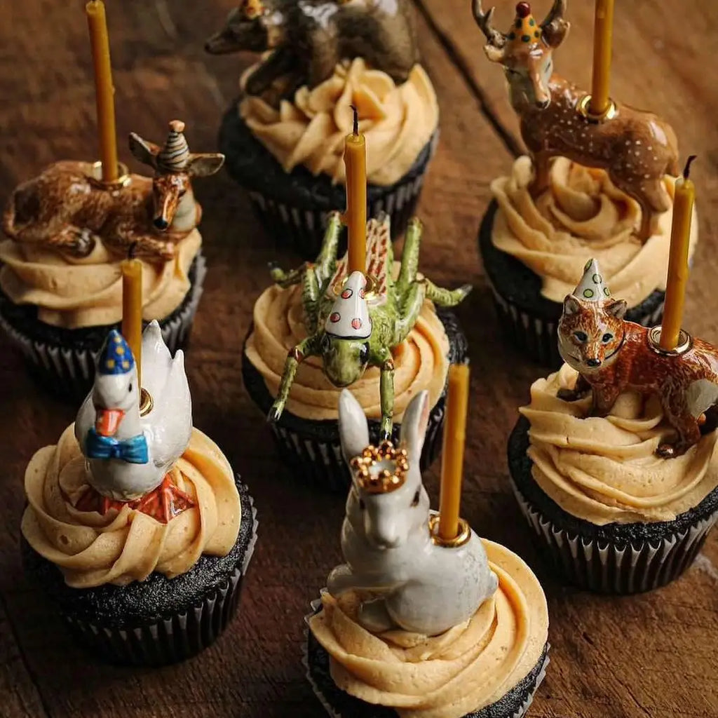 A set of six intricately decorated cupcakes, each topped with a Cricket Cake Topper wearing a party hat and a birthday candle, sitting on a wooden surface.