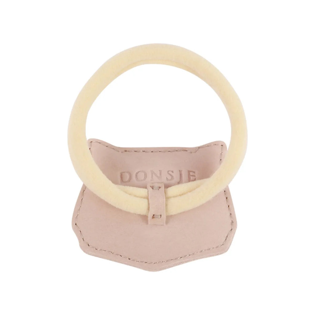 A pale pink Donsje Leather Hair Tie - Cat designed as a soft, circular band with fuzzy fabric on top, attached to a small premium leather base with a buckle detail.