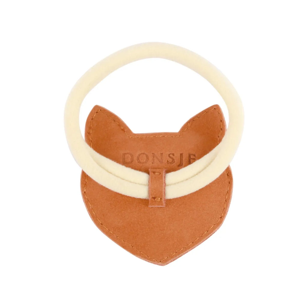 A whimsical children's accessory featuring a tan premium leather fox-shaped bib with the brand "Donsje" embossed on it, complemented by a cream-colored elastic band.