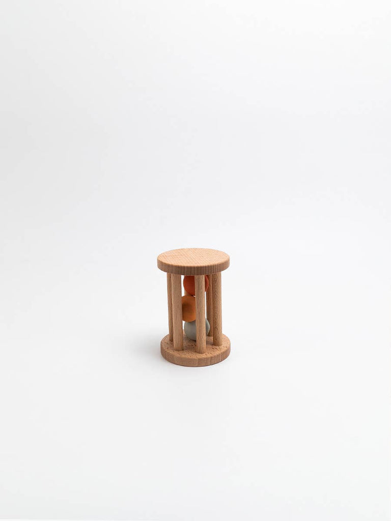 The Sabo Concept Rolling Rattle - Lagoon is a small handmade wooden baby toy with cylindrical bars and two colored balls inside, shown on a plain white background.