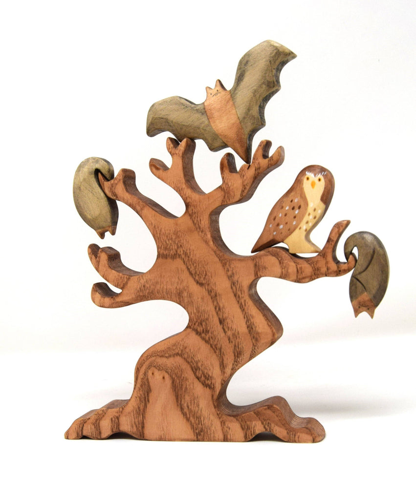 The Handmade Wooden Little Owl is a wooden puzzle sculpture of a tree with green leaves, featuring a handcrafted owl perched on one branch and a bat hanging from another, all in natural wood tones with plant-based stains.