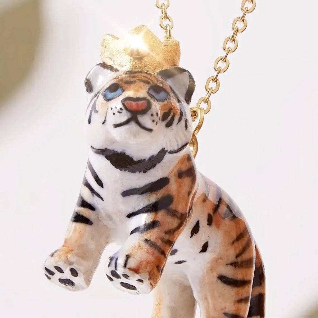 A close-up photo of a small Tiger King Necklace, featuring hand-painted stripes and a golden crown, hanging from a 24k gold-plated chain against a soft white background.